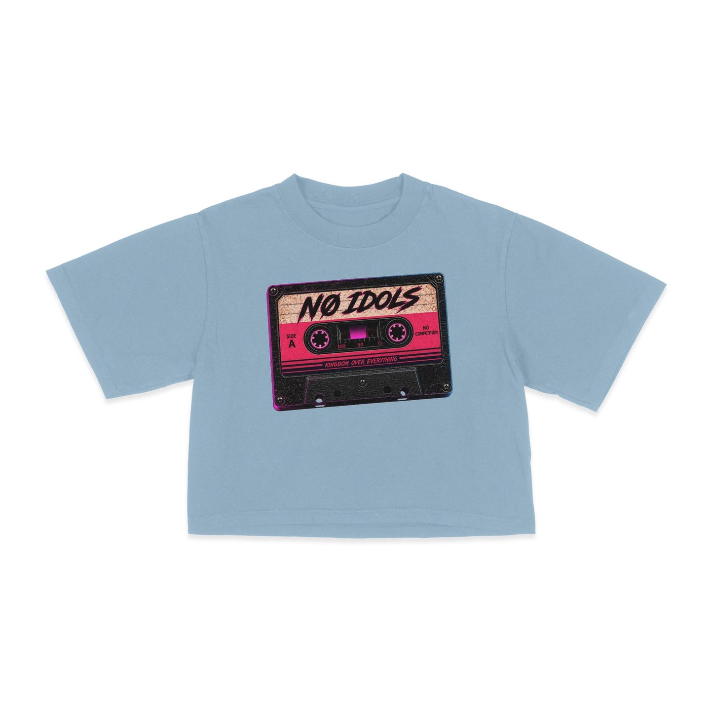 A light blue short-sleeve crop top t-shirt featuring a graphic print of a retro cassette tape with the text 'NO IDOLS' in black script on a pink and beige cassette body, displayed on a clean white background.