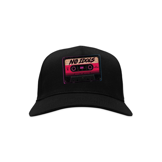 A black baseball cap featuring a rectangular patch on the front with a retro cassette tape graphic in pink, beige, and black, with the text 'NO IDOLS' written across it.