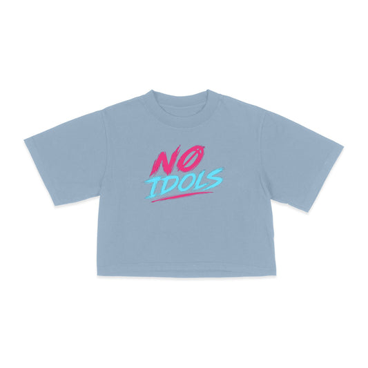 A light blue short-sleeve crop top t-shirt with a graphic on the chest reading 'NO IDOLS' in pink and light blue, displayed on a clean white background.