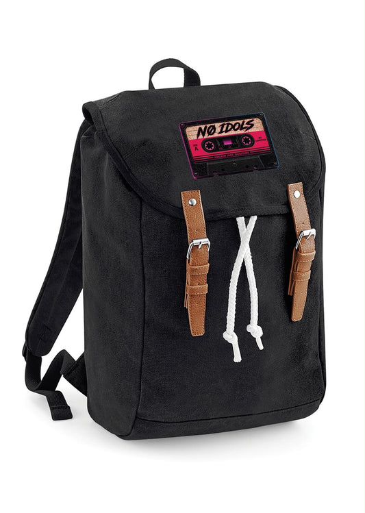 A black canvas backpack with a top flap, brown faux-leather strap details, a white drawstring, and a cassette tape patch on the front that reads 'NO IDOLS'.