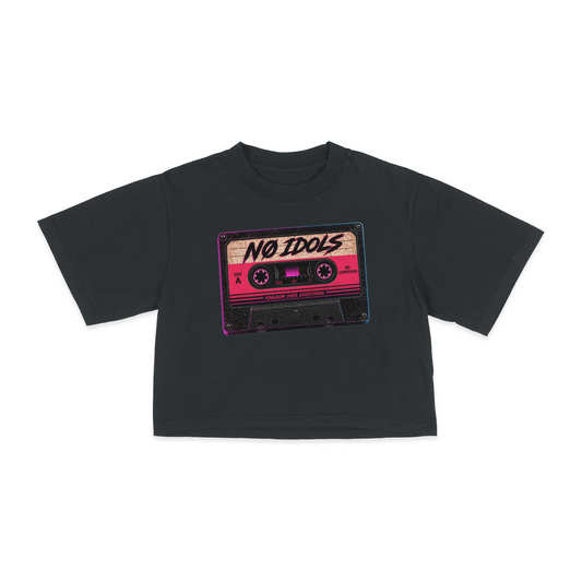 A black short-sleeve crop top t-shirt featuring a retro cassette tape graphic on the chest with the text 'NO IDOLS' in stylized lettering.